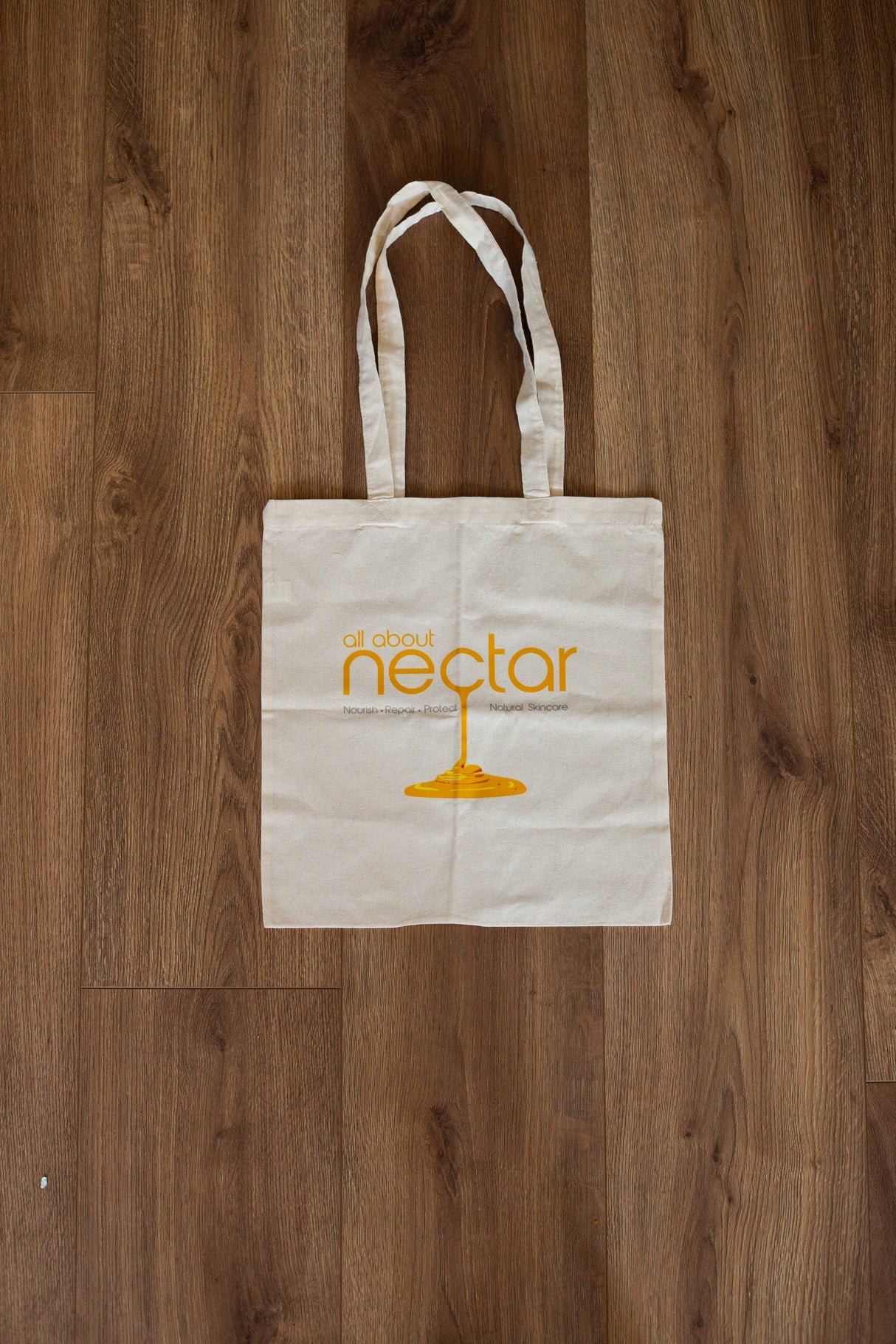 White tote bag with 'all about nectar' logo on a wooden surface