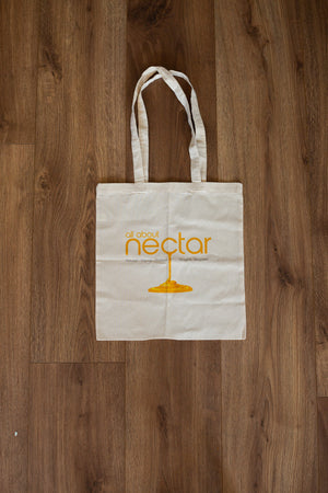White tote bag with 'all about nectar' logo on a wooden surface