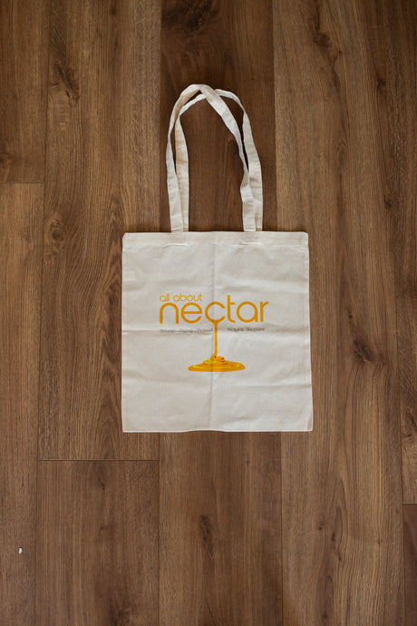White tote bag with 'all about nectar' logo on a wooden surface